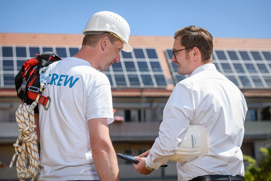 Zwei Männer mit Solarpanels im Hintergrund (Foto)